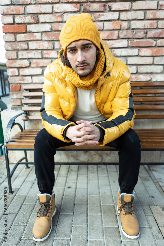 Fashionable handsome man sits on the bench in winter time Fashionable handsome man sits on the bench in winter time