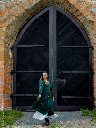 beautiful brunette woman in long green vintage dress posing in ancient castle 
