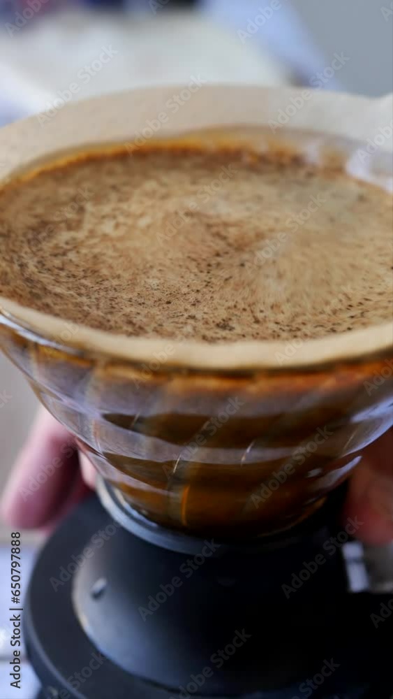 A man's hand shakes brewed coffee using the drip method in a filter cup for a better result. The barista shook the brewed coffee foam drink with his hand. Alternative brewing method. Vertical video A man's hand shakes brewed coffee using the drip method in a filter cup for a better result. The barista shook the brewed coffee foam drink with his hand. Alternative brewing method. Vertical video