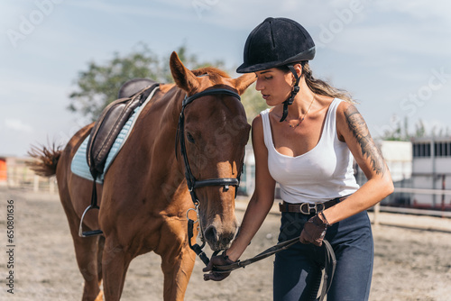 Young jockey pulling the rope that ties her horse in the riding arena. Middle-aged woman leading her equine animal on a leash to finish riding class.