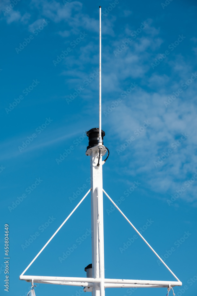 A metallic nautical light pole against a bright blue sky. Maritime radio antenna installation on the ship.