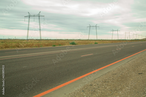 Electric transmission lines along the highway in the steppe against the background of the evening cloudy sky
