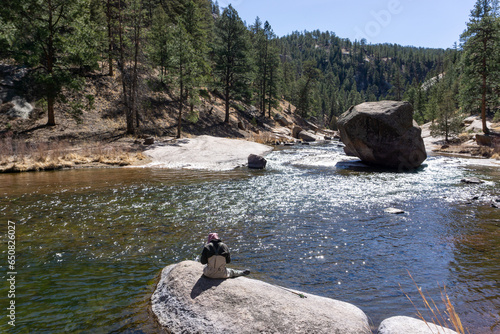 Young woman sits on a rock while fishing in Chesman canyon Colorado