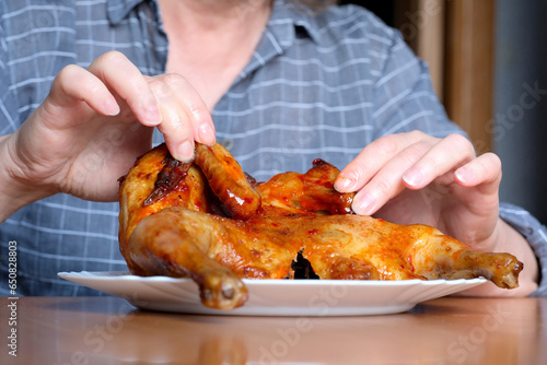 The hands of an elderly woman operate a grilled chicken