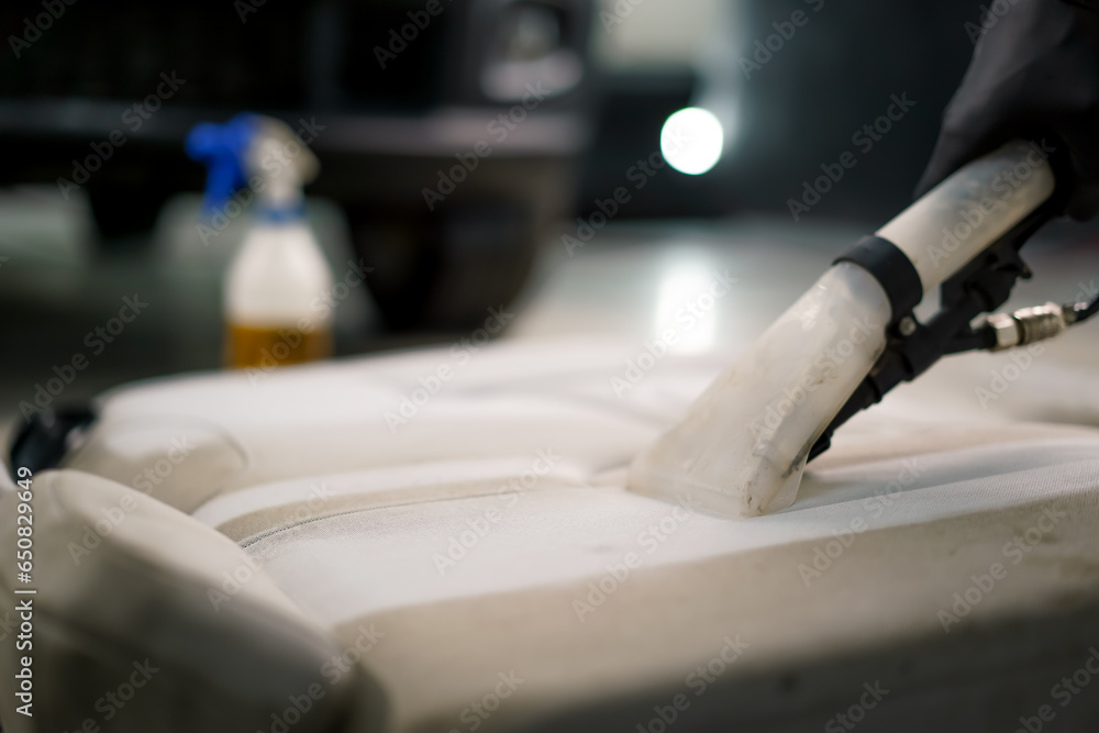 A close-up of a car wash worker using a vacuum cleaner to clean white car seats in the process of detangling