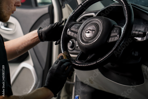Close-up of a car wash worker cleaning the steering wheel of a luxury car with a brush and washing foam in the process of detangling © Guys Who Shoot