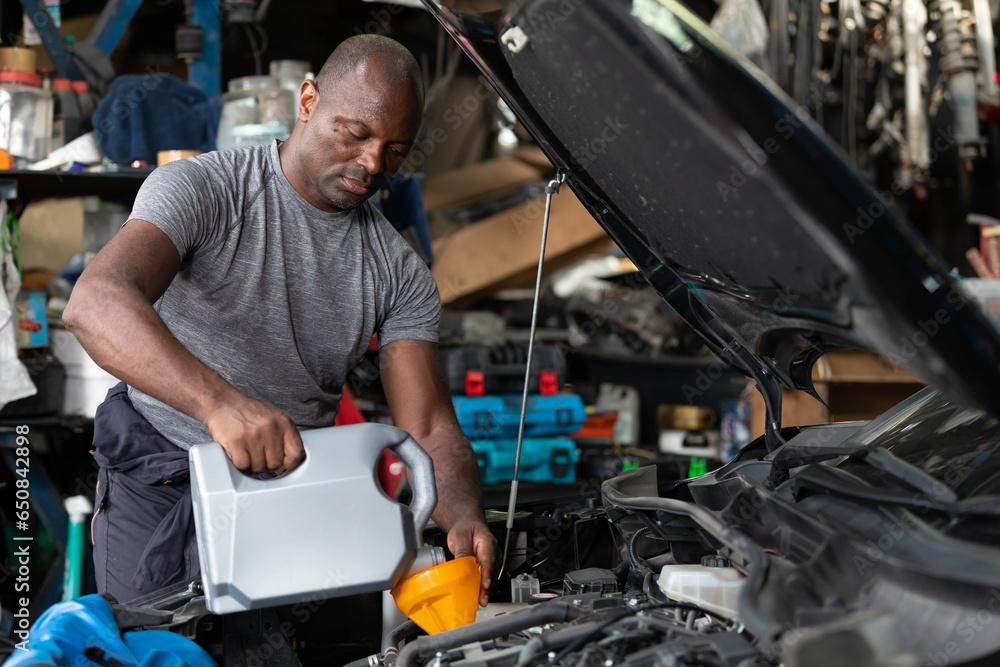 African mechanic worker filling engine oil into a car in garage African mechanic worker filling engine oil into a car in garage