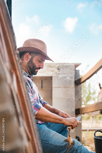western man sharpening a stick surrounded by horses on his ranch