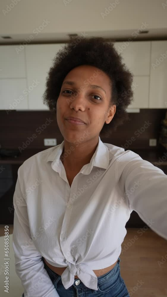 POV of attractive curly black female using smartphone holding selfie pose at home, smiling looking at camera. Vertical portrait of pretty African woman taking video selfies on smartphone indoors. POV of attractive curly black female using smartphone holding selfie pose at home, smiling looking at camera. Vertical portrait of pretty African woman taking video selfies on smartphone indoors.