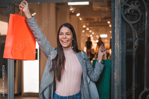 Beautiful smiling woman in her thirties feeling cheerful, accomplished and excited while exiting the shopping store with several paper bags. Satisfied female after shopping in a shopping mall.