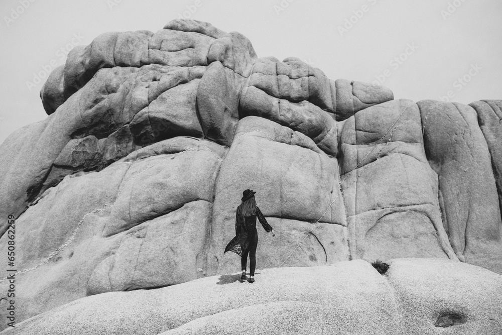 Woman in a black outfit and black hat walking through a rocky desert landscape Woman in a black outfit and black hat walking through a rocky desert landscape
