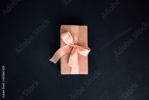 Background for greetings. Gifts wrapping in soft pink paper with pink ribbon on a black concrete background. Top view