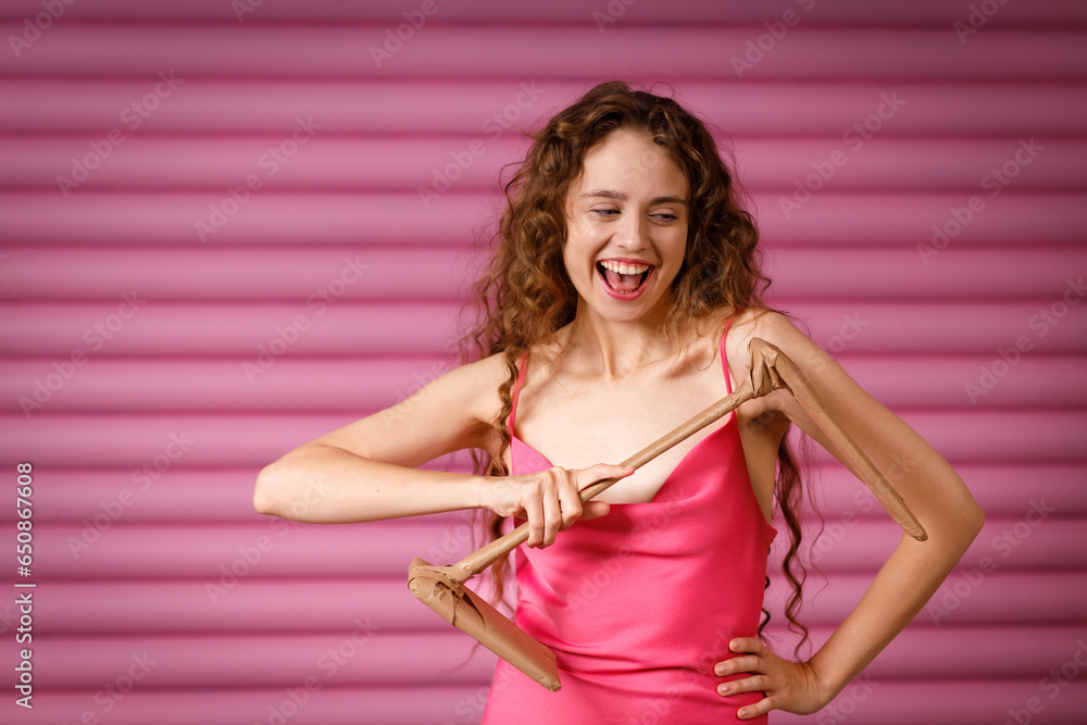 Young positive smiling woman receives a gift and holds in her hands a table electric lamp wrapped in rustic beige craft paper on pink background. Black Friday concept.