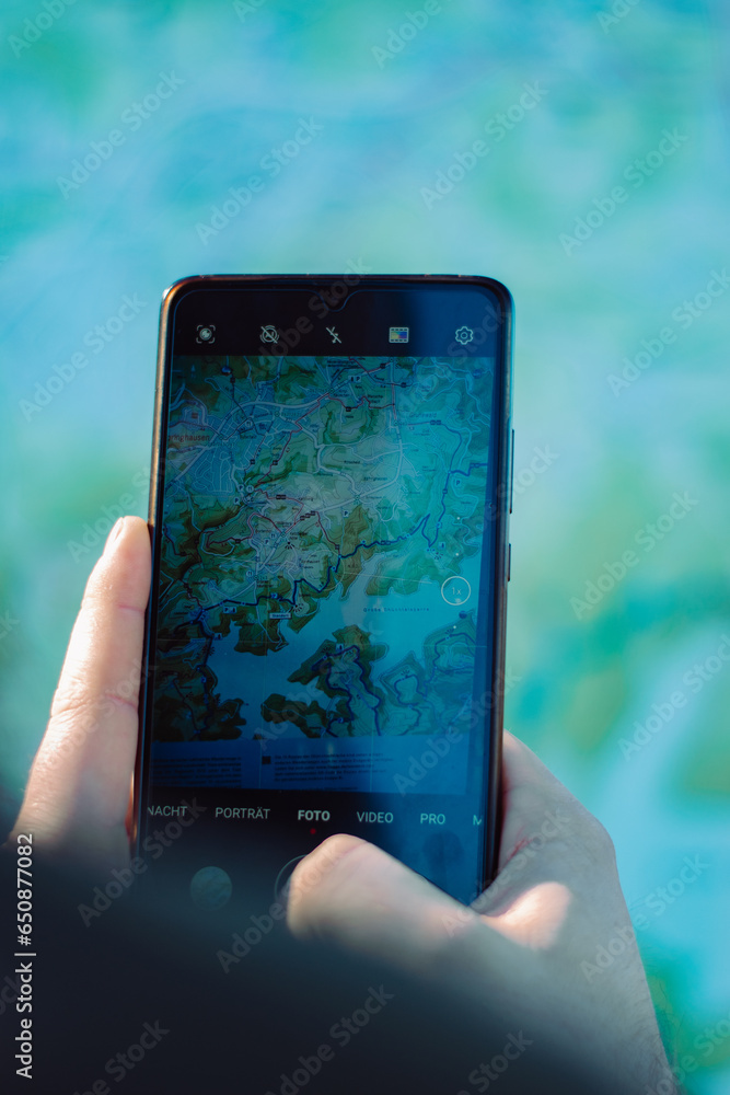 Vertical shot of a hand holding a smartphone and taking a photo of a map Vertical shot of a hand holding a smartphone and taking a photo of a map