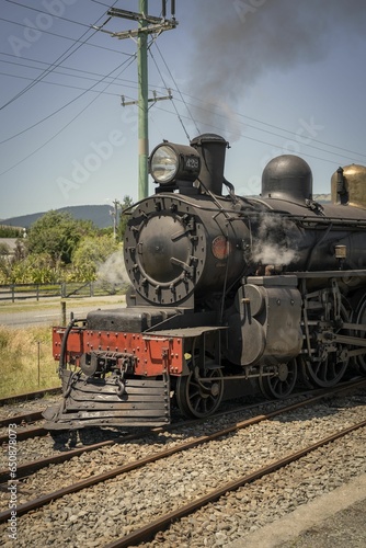 Aged, corroded train engine travels along a track in a train yard with a plume of smoke