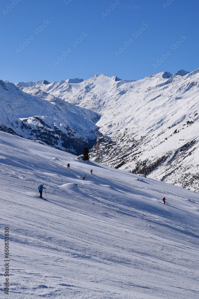 Skiers and snowboarders in Hochgurgl ski resort, backdropped by the Ötztal valley and the snow capped alpine mountains in Tyrol, Austria on a beautiful sunny day, perfect conditions for winter sports.