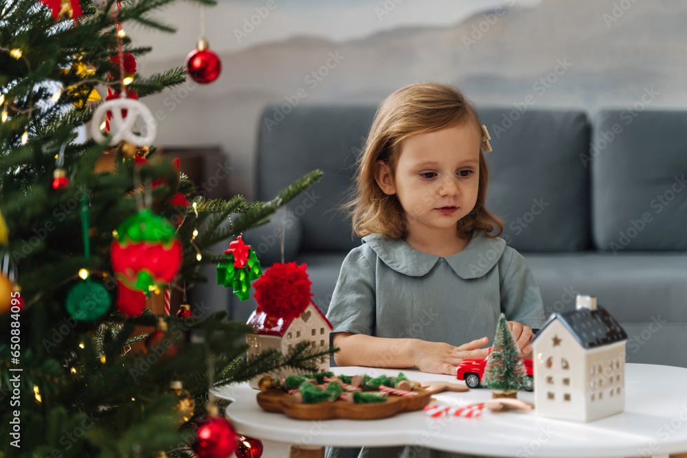 Christmas holidays. A little girl plays with toy cars, little houses and christmas decorations. Holiday Activity for Kids. Merry Christmas and Happy Holidays!