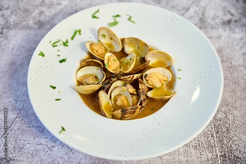 Plate of steamed clams served in a rich, aromatic brown sauce with a sprinkling of herbs for flavor