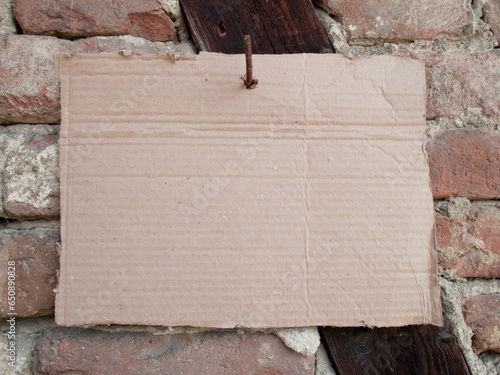 Photography Close-up of a piece of cardboard hanging from a nail in front of an old stone wa