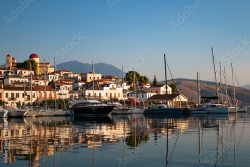 Fleet of sailboats moored in a tranquil harbor near a city skyline after sunrise in Galixidi, Greece