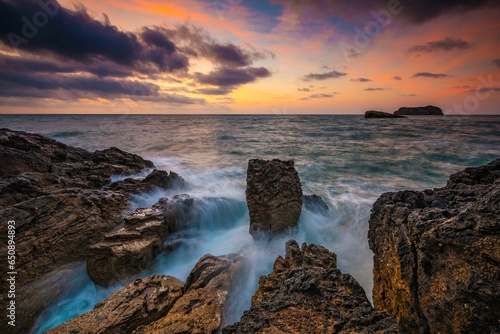 Scenic seascape at sunset with coastal rocks in the foreground.