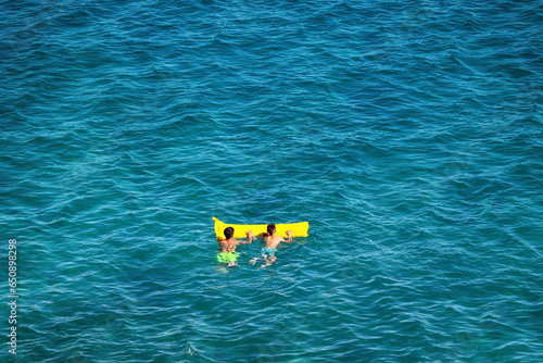 Młoda dziewczyna w stringach płynie na materacu po morzu.