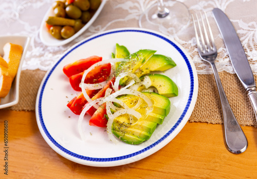 Salad of tomatoes, avocado, white onion, flavored with olive oil and herbs. Light buffet vegetable snack, slices of bread and glass of wine are waiting on table.