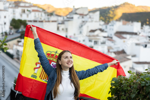 Cheerful young female traveler waving Spanish flag on city street, sport fan supporter