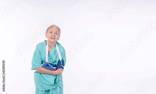 Accident injury elderly woman 70s patient gown suffering broken arm soft splint standing over isolated white background.Painful older female stress problems cramp arm broken. Insurance accident health