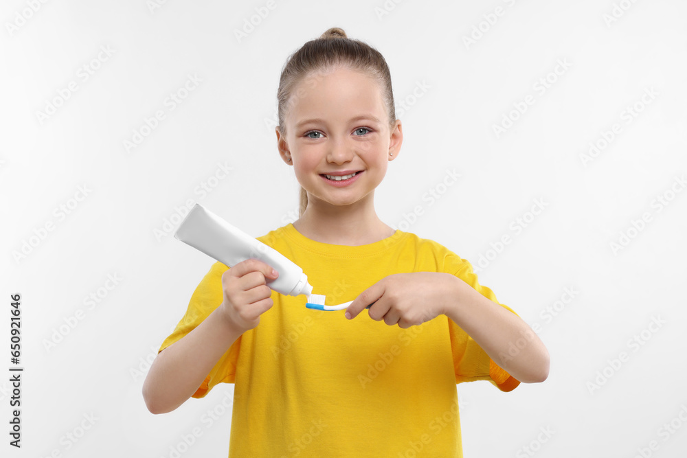 Happy girl squeezing toothpaste from tube onto toothbrush on white background Happy girl squeezing toothpaste from tube onto toothbrush on white background