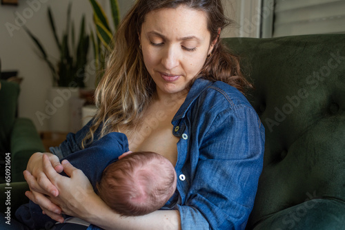 Mother breastfeeding her baby son while sitting on armchair at home