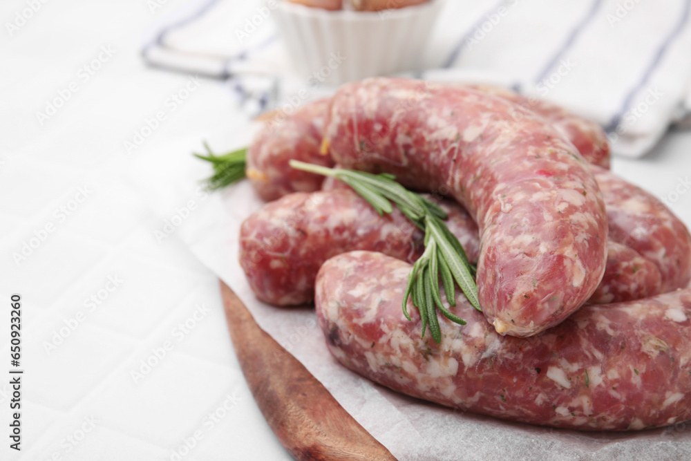 Raw homemade sausages and rosemary on white table, closeup. Space for text