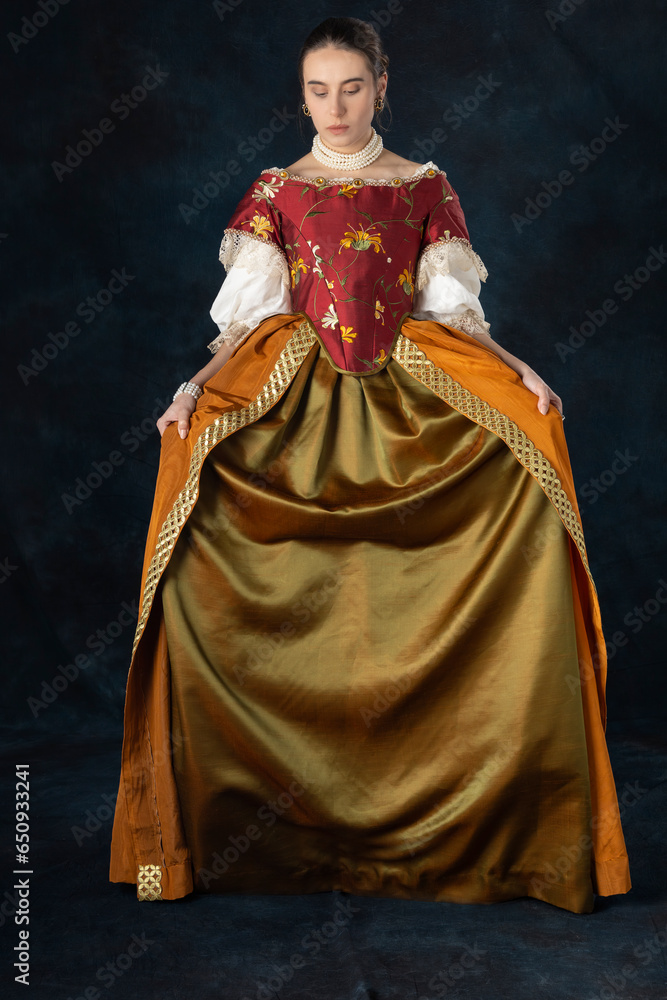 Woman wearing a Renaissance, Tudor, Georgian, or high fantasy costume with a red embroidered bodice and a pearl choker