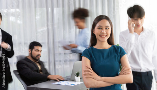 Young Asian businesswoman portrait poses confidently with diverse coworkers in busy meeting room in motion blurred background. Multicultural team works together for business success. Concord © Summit Art Creations
