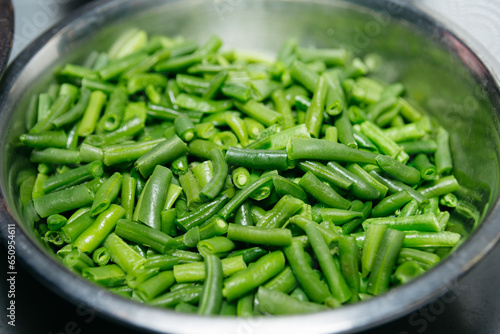 Green beans in a metal bowl on a kitchen table, close up. Fresh and juicy beans, raw ingredient before preparing dish.