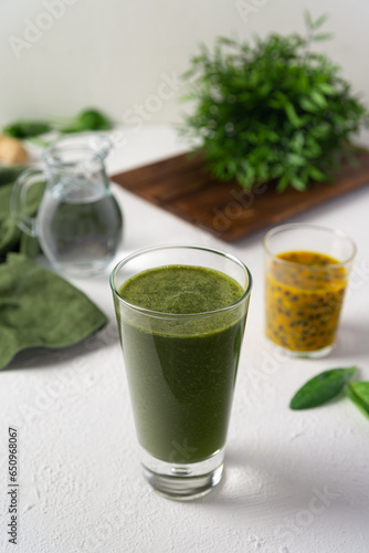 A green smoothie alongside passion fruit pulp and spinach leaves and a pitcher of water. Healthy green smoothie, refreshing diet drink on a white background.