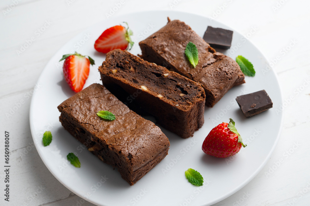 Chocolate brownie cut into portions and decorated with strawberries and mint.