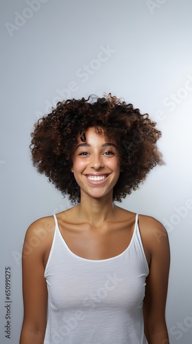 Image of smiling confident young woman in white T-shirt looking at camera isolated in grey background