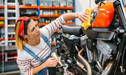 Concentrated mechanic woman cleaning fuel tank of custom motorcycle with a microfiber cloth and polish after repair on factory