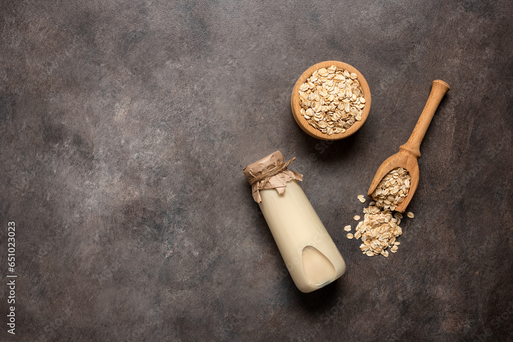 Oat milk in a bottle and oat flakes on a brown rustic background. Top view, flat lay, copy space.