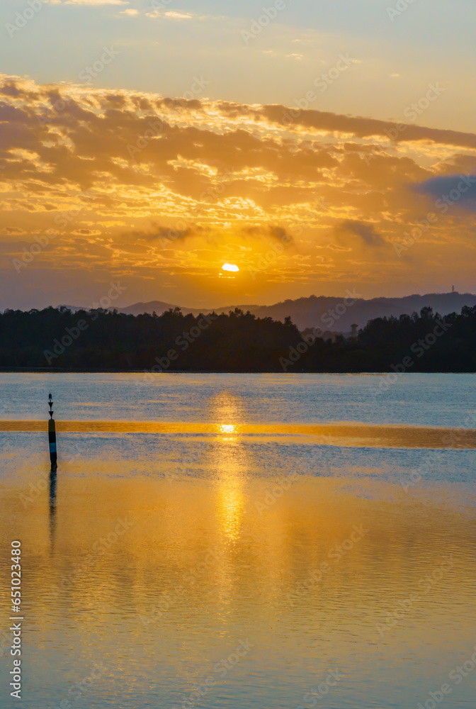 Golden sunrise waterscape with a scattering of clouds and reflections as the sun comes up