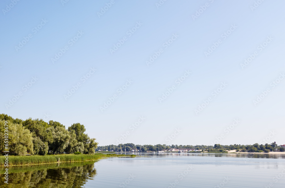 Scenery with dense trees near the river in Kyiv, Europe. Pier with parked yachts on background