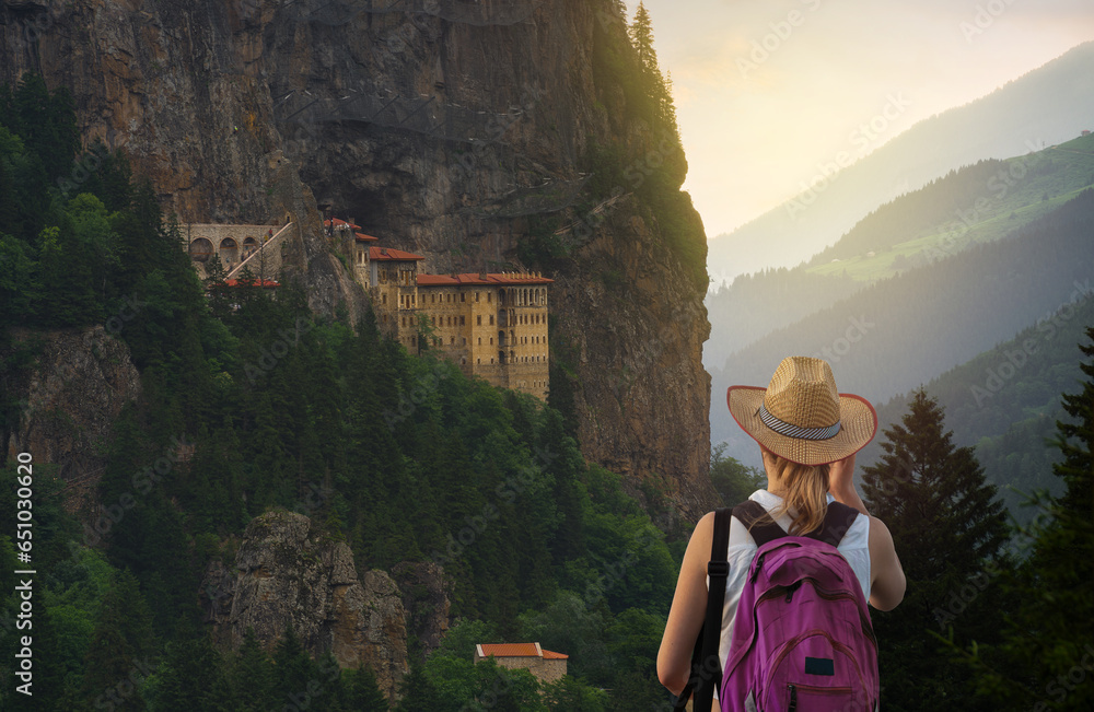 Tourist woman watches Sümela Monastery at sunset time. Sumela Monastery is one of the best tourist travel destinations in the Black Sea region of Turkey. Macka town, Trabzon , Turkey  - obrazy, fototapety, plakaty 