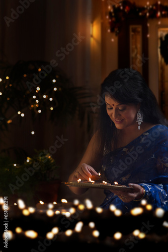 Beautiful indian woman in traditional sari arranging oil lamp during diwali festival photo