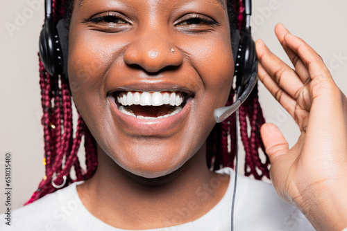 Close up shot portrair of delighted smiley cheerful African American woman with braids wearing wireless headset headphones supporting people online receiving call from customers. photo