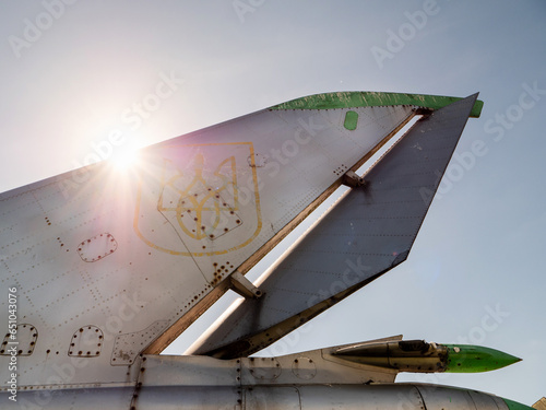 Military war jet airplane tail with Ukrainian air defense logo against blue sky. Old, worn out and rough shiny metal surface. Heavy duty airplane with many combat missions photo