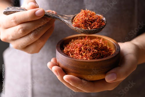 Canvas-taulu Dried safflower in wooden bowl and spoon holding by hand, Herbal tea