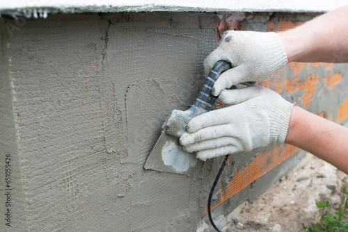 A builder is plastering a house. Finishing the house with concrete. Applying plaster to the foundation