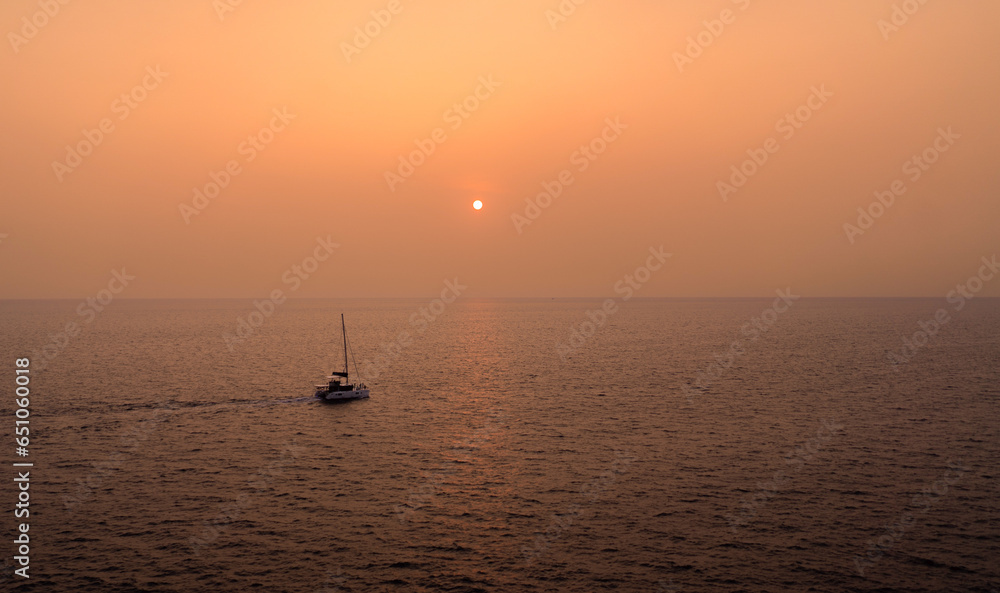 
sunset at sea A sailboat floats on the surface of the water and there is a reflection of the orange sun in the evening.