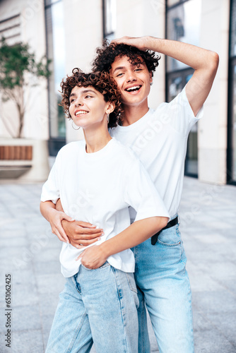 Young smiling beautiful woman and her handsome boyfriend in casual summer white t-shirt and jeans clothes. Happy cheerful family. Female having fun. Couple posing in the street background at sunny day © halayalex